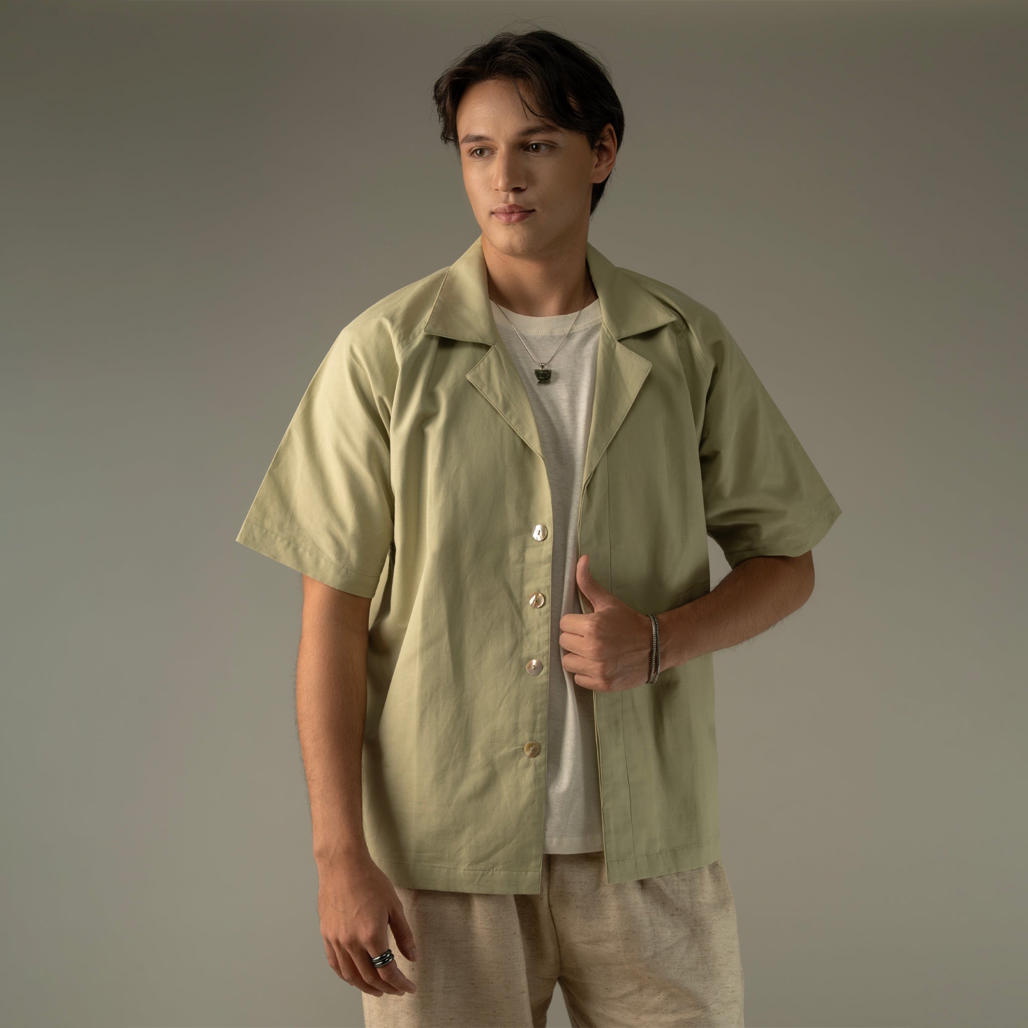 Man wearing a light green shirt over a white t-shirt on a plain background